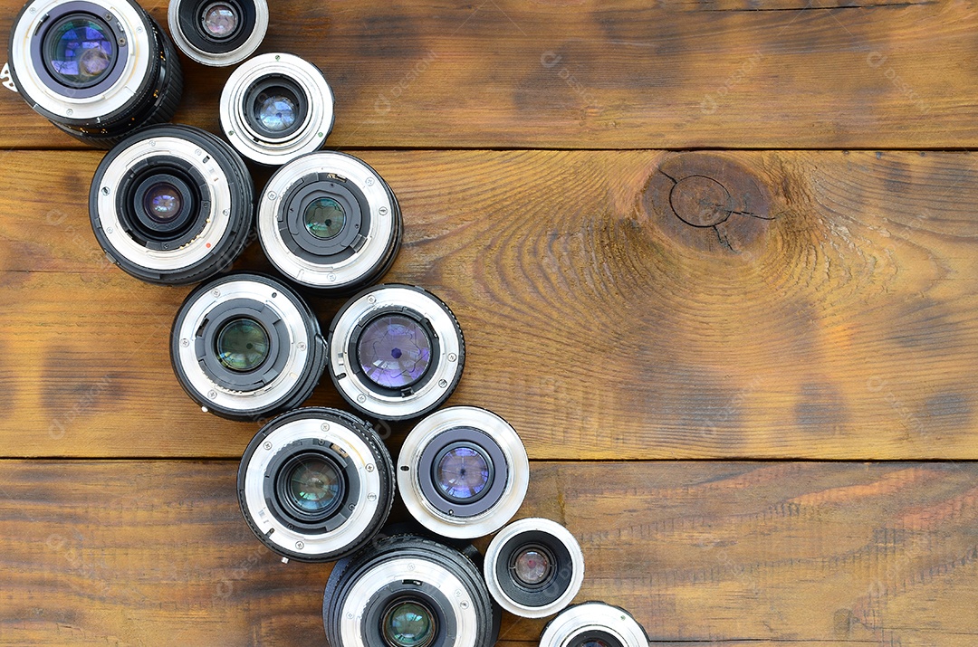 Várias lentes fotográficas repousam sobre um fundo de madeira marrom