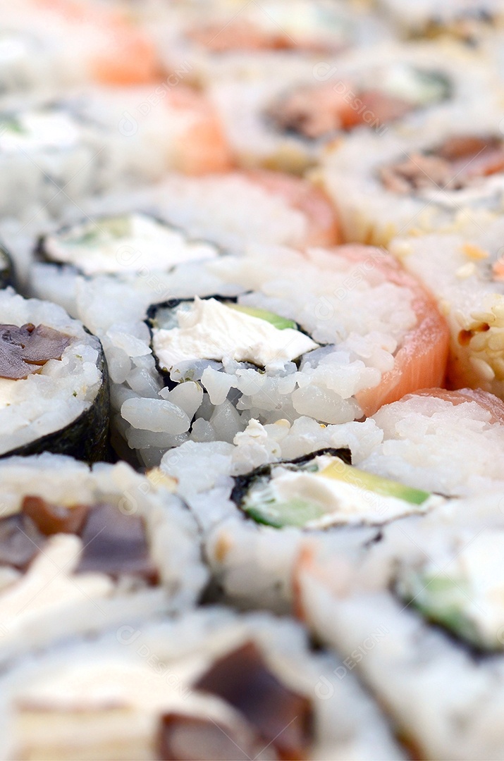 Um conjunto de sushi com vários rolinhos está localizado em uma tábua de corte de madeira sobre uma mesa na cozinha de um sushi barr