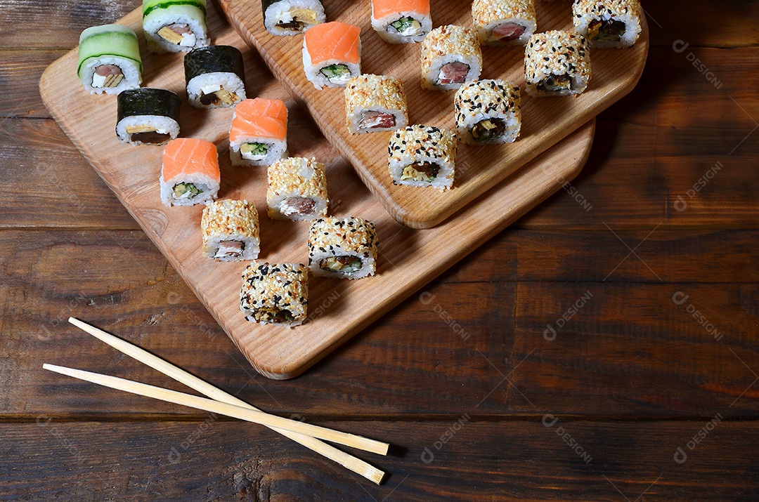 Um conjunto de sushi com vários rolinhos está localizado em uma tábua de corte de madeira sobre uma mesa na cozinha de um sushi barr