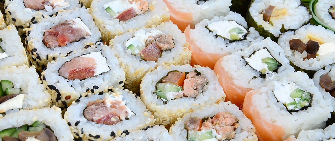 Um conjunto de sushi com vários rolinhos está localizado em uma tábua de corte de madeira sobre uma mesa na cozinha de um sushi barr