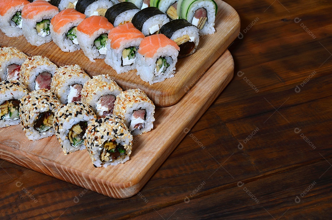 Um conjunto de sushi com vários rolinhos está localizado em uma tábua de corte de madeira sobre uma mesa na cozinha de um sushi barr