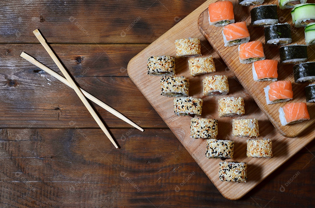 Um conjunto de sushi com vários rolinhos está localizado em uma tábua de corte de madeira sobre uma mesa na cozinha de um sushi barr