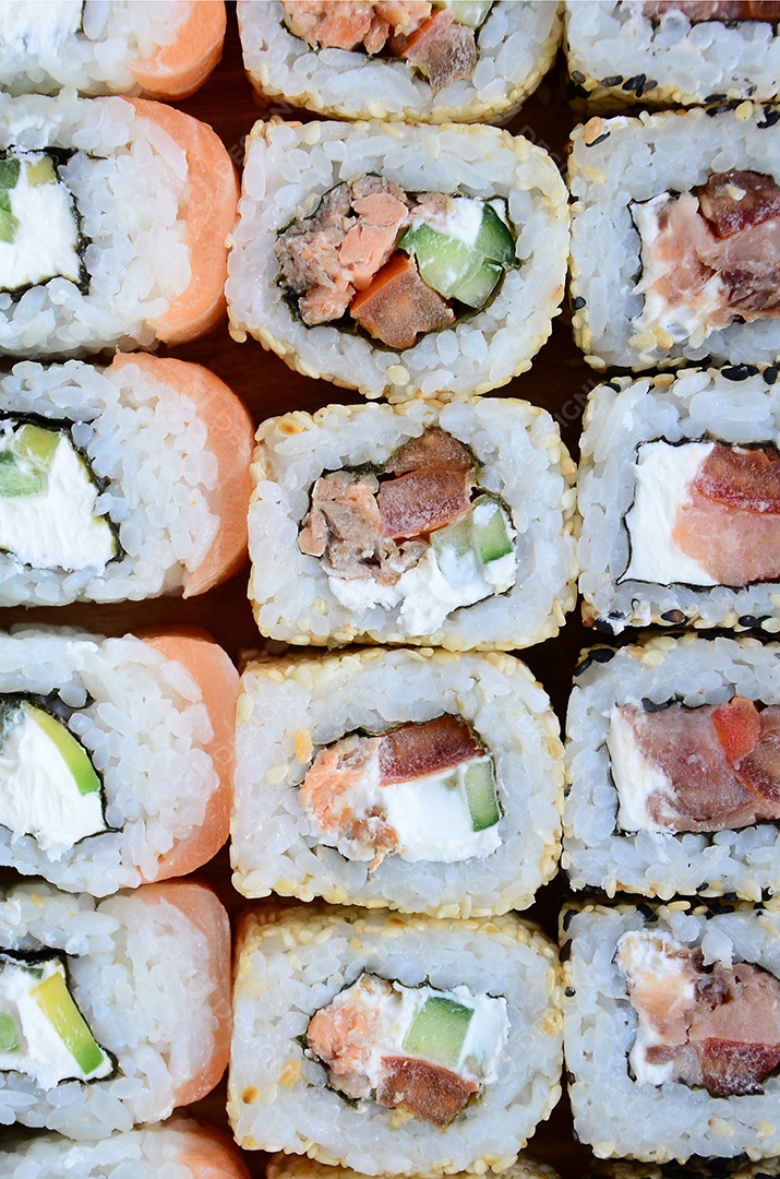 Um conjunto de sushi com vários rolinhos está localizado em uma tábua de corte de madeira sobre uma mesa na cozinha de um sushi barr