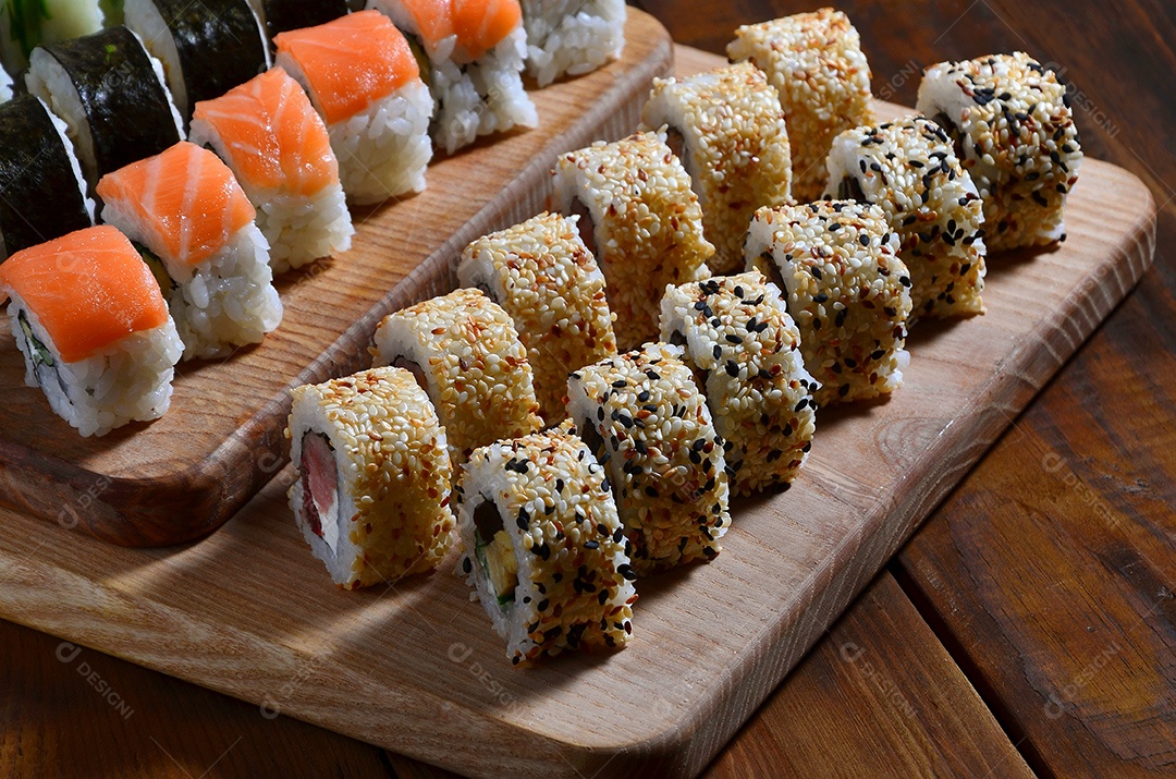 Um conjunto de sushi com vários rolinhos está localizado em uma tábua de corte de madeira sobre uma mesa na cozinha de um sushi barr