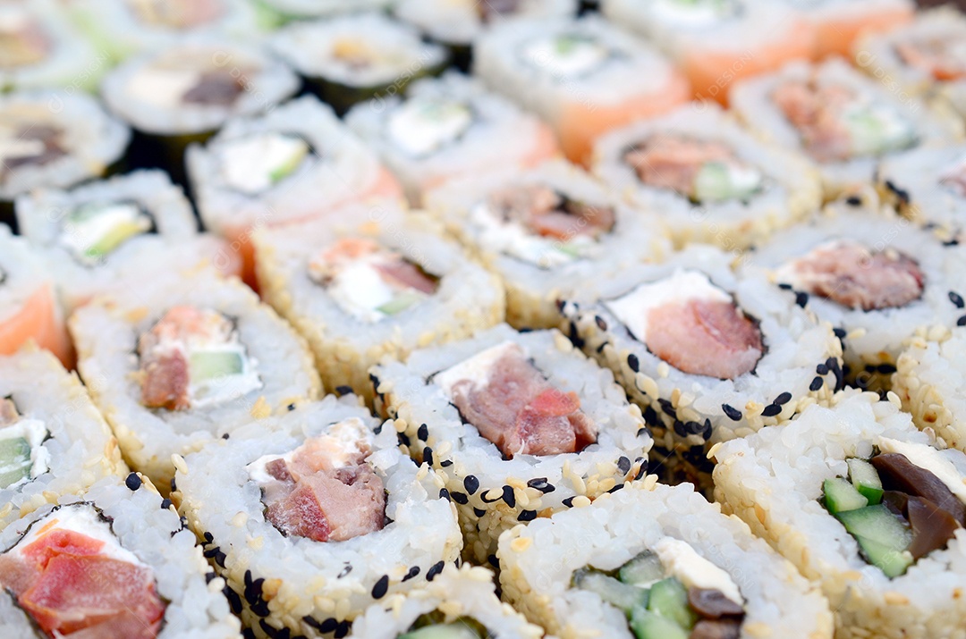 Um conjunto de sushi com vários rolinhos está localizado em uma tábua de corte de madeira sobre uma mesa na cozinha de um sushi barr