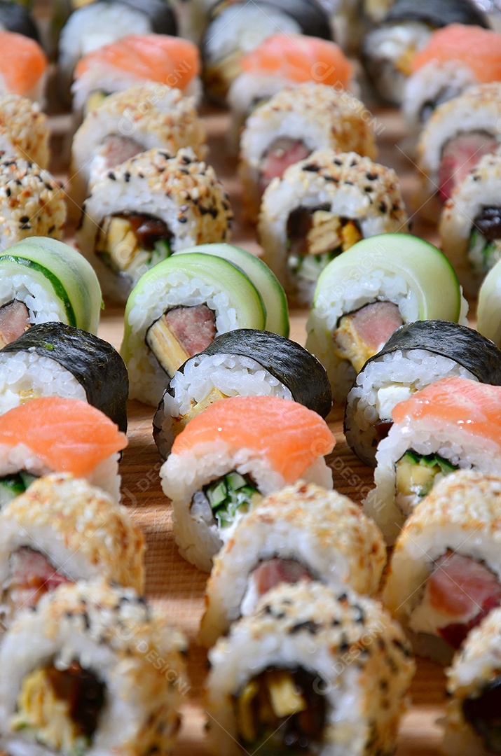 Um conjunto de sushi com vários rolinhos está localizado em uma tábua de corte de madeira sobre uma mesa na cozinha de um sushi barr