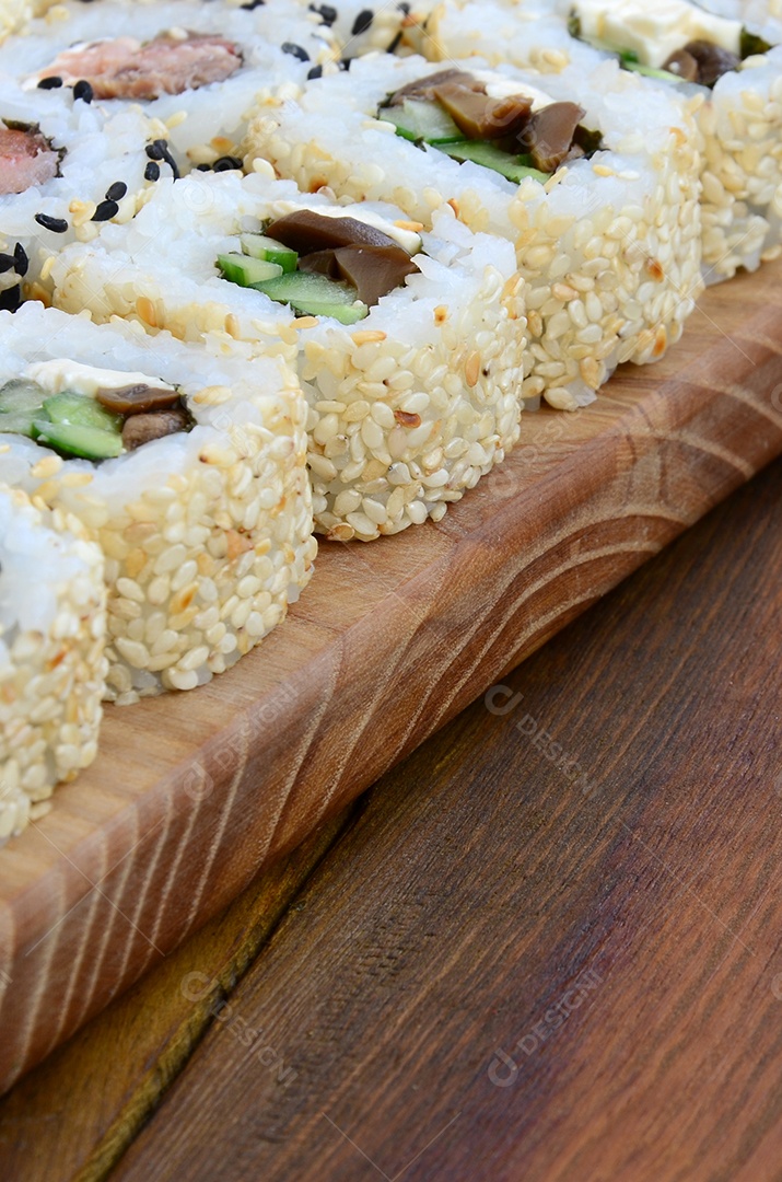 Um conjunto de sushi com vários rolinhos está localizado em uma tábua de corte de madeira sobre uma mesa na cozinha de um sushi barr