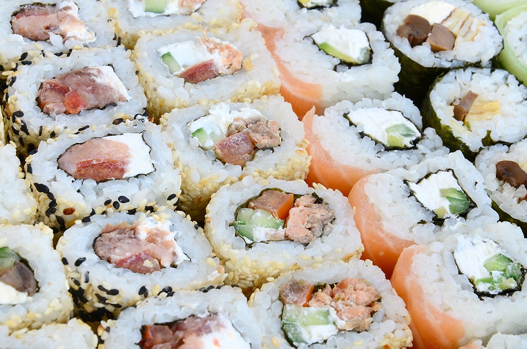 Um conjunto de sushi com vários rolinhos está localizado em uma tábua de corte de madeira sobre uma mesa na cozinha de um sushi barr