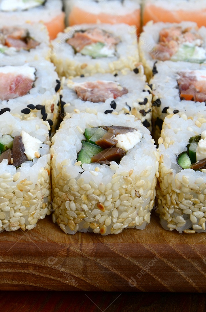 Um conjunto de sushi com vários rolinhos está localizado em uma tábua de corte de madeira sobre uma mesa na cozinha de um sushi barr