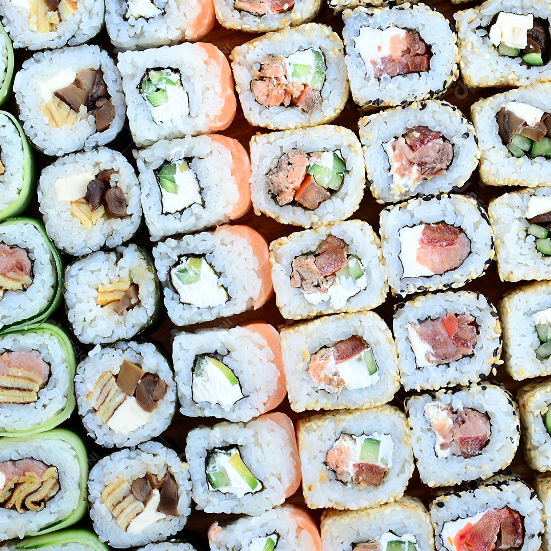 Um conjunto de sushi com vários rolinhos está localizado em uma tábua de corte de madeira sobre uma mesa na cozinha de um sushi barr