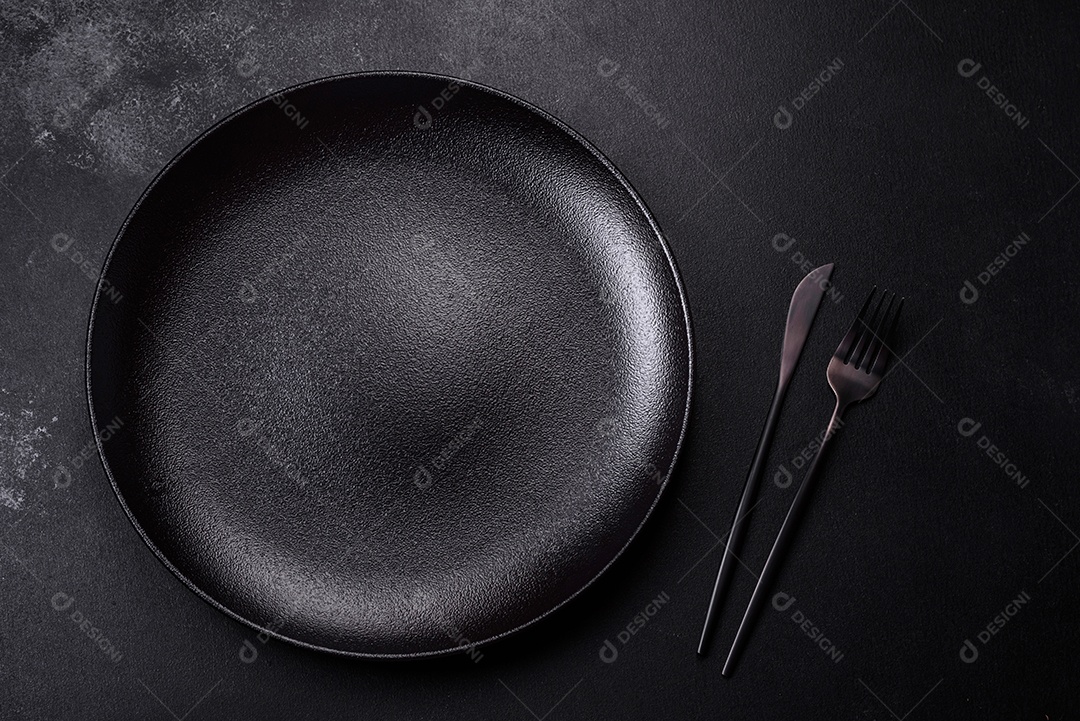 Placa cerâmica preta vazia sobre um fundo escuro de concreto. Preparando a mesa para um jantar em família