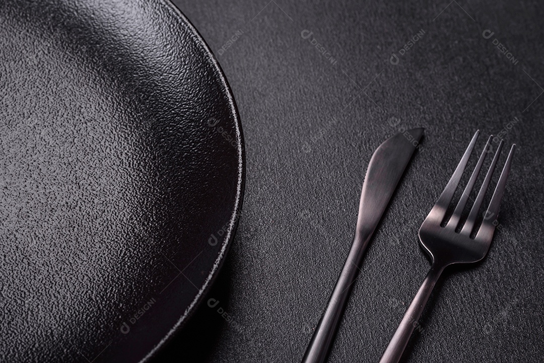 Placa cerâmica preta vazia sobre um fundo escuro de concreto. Preparando a mesa para um jantar em família