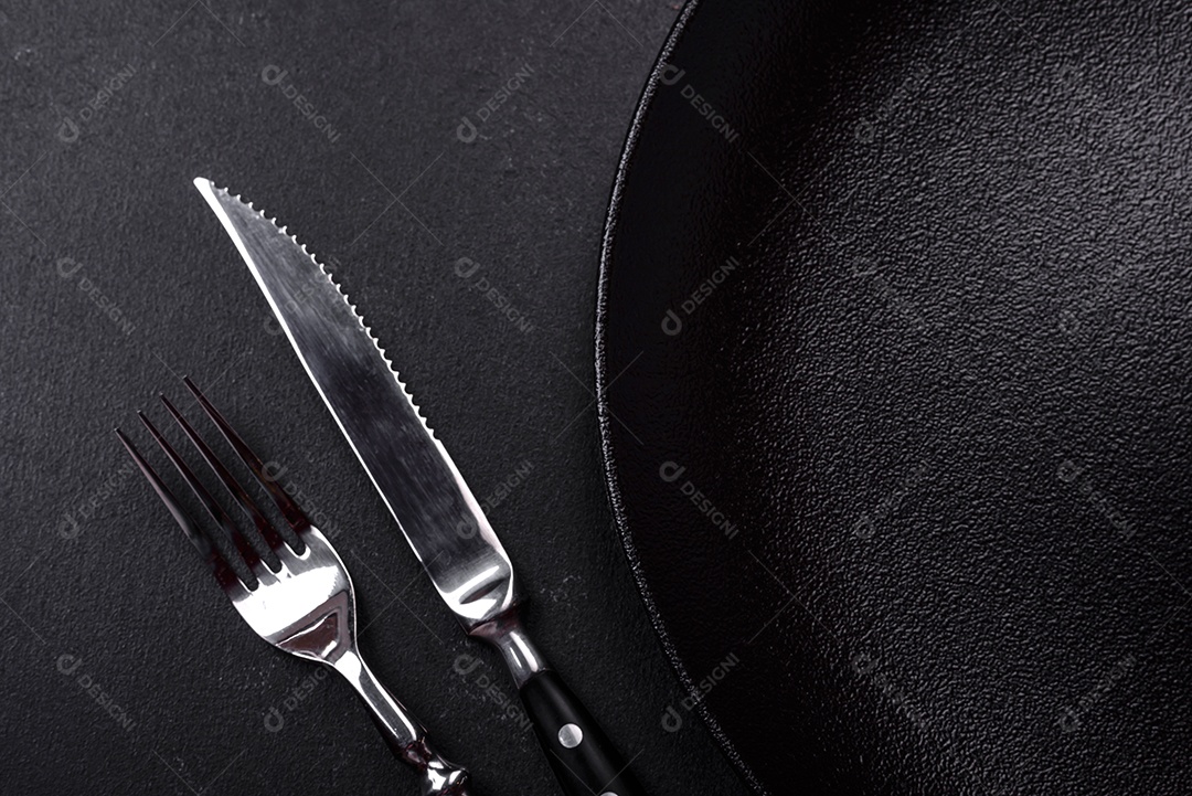 Placa cerâmica preta vazia sobre um fundo escuro de concreto. Preparando a mesa para um jantar em família