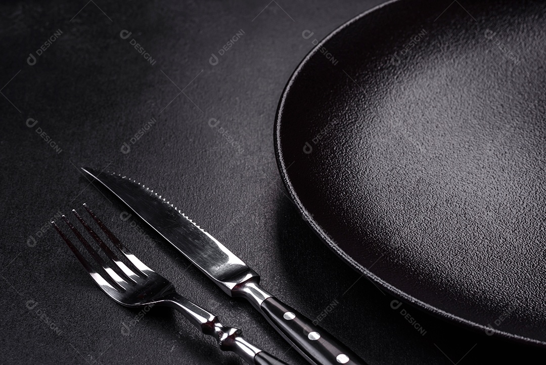 Placa cerâmica preta vazia sobre um fundo escuro de concreto. Preparando a mesa para um jantar em família