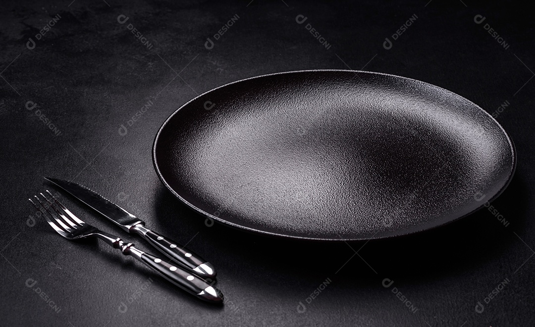 Placa cerâmica preta vazia sobre um fundo escuro de concreto. Preparando a mesa para um jantar em família