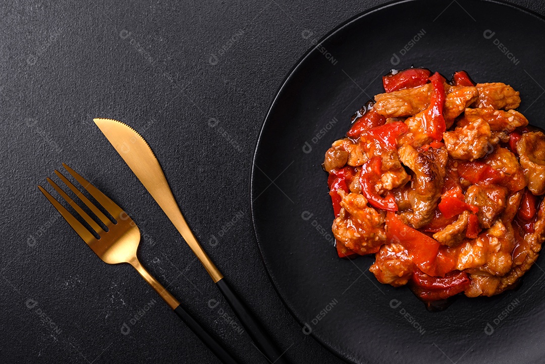Deliciosa carne suculenta com pimenta e molho em uma placa de cerâmica preta sobre um fundo escuro de concreto