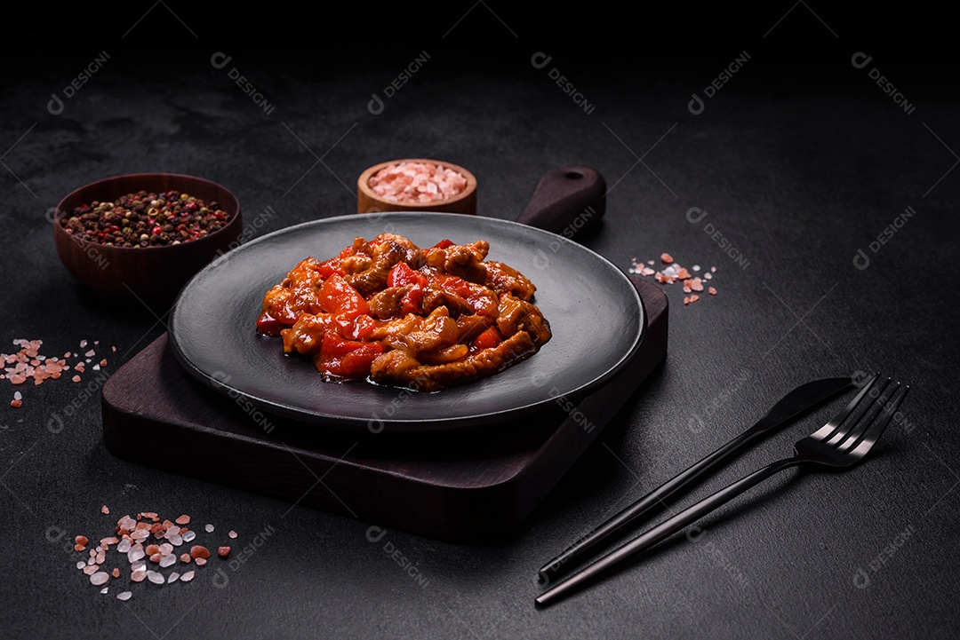 Deliciosa carne suculenta com pimenta e molho em uma placa de cerâmica preta sobre um fundo escuro de concreto