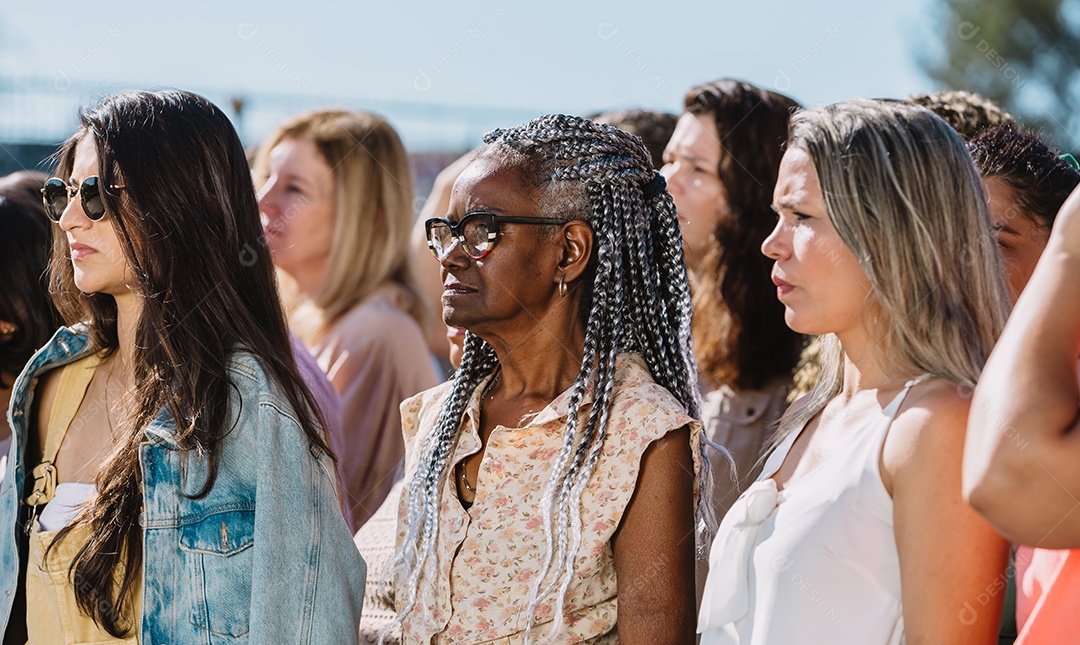 Grupo de mulheres ao ar livre, olhando para frente com uma expressão séria. Manifestantes, direitos das mulheres.