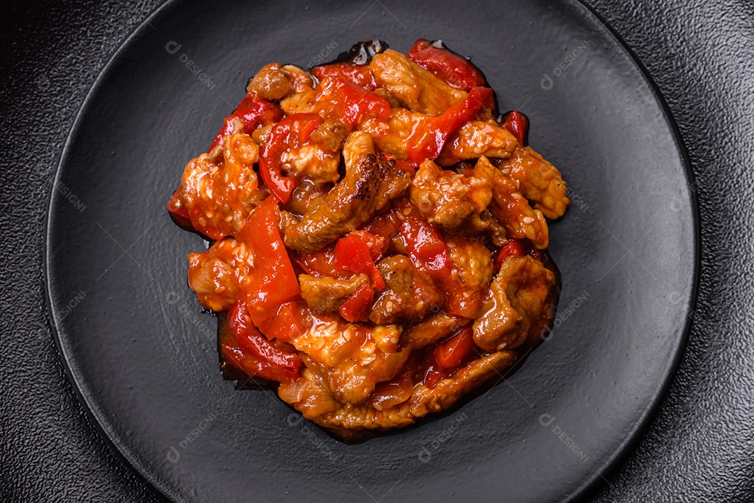 Deliciosa carne suculenta com pimenta e molho em uma placa de cerâmica preta sobre um fundo escuro de concreto