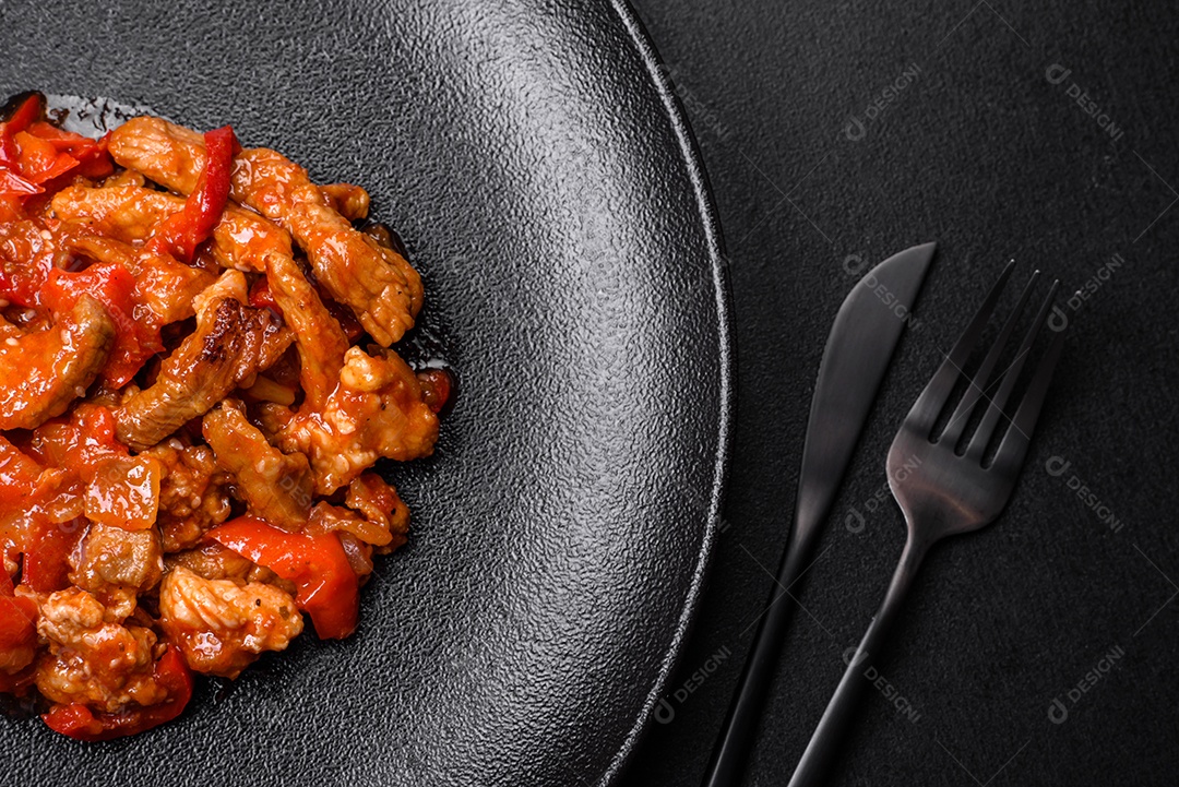 Deliciosa carne suculenta com pimenta e molho em uma placa de cerâmica preta sobre um fundo escuro de concreto