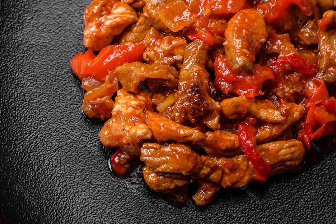 Deliciosa carne suculenta com pimenta e molho em uma placa de cerâmica preta sobre um fundo escuro de concreto