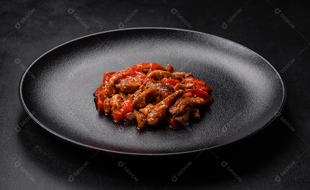 Deliciosa carne suculenta com pimenta e molho em uma placa de cerâmica preta sobre um fundo escuro de concreto