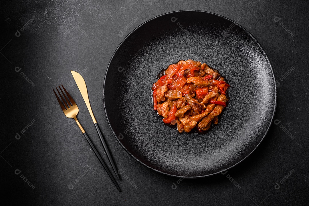 Deliciosa carne suculenta com pimenta e molho em uma placa de cerâmica preta sobre um fundo escuro de concreto