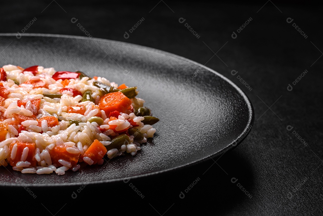 Delicioso risoto fresco com legumes, especiarias e ervas em uma placa preta sobre um fundo escuro de concreto