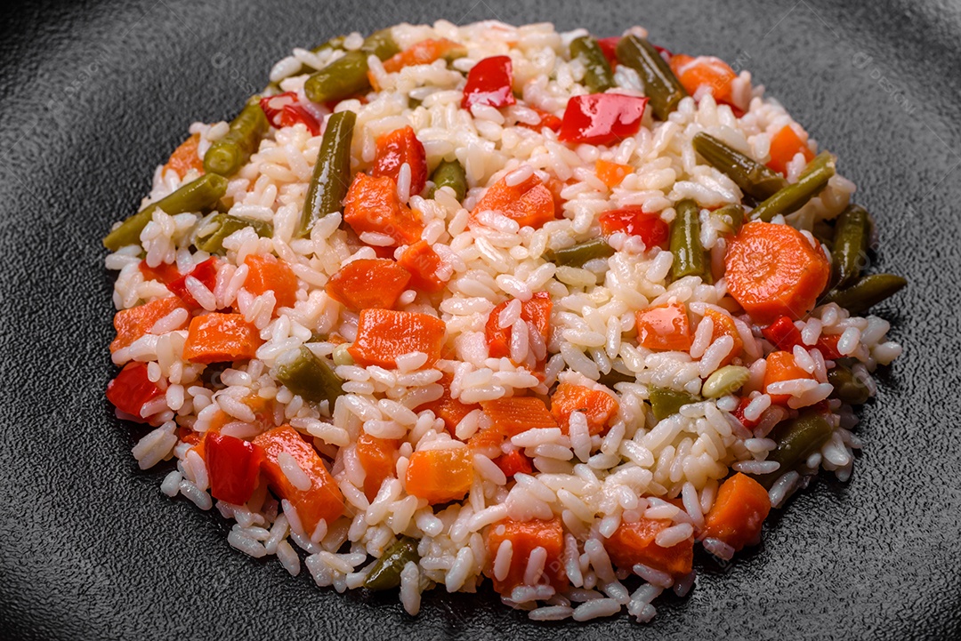 Delicioso risoto fresco com legumes, especiarias e ervas em uma placa preta sobre um fundo escuro de concreto