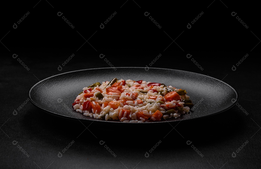 Delicioso risoto fresco com legumes, especiarias e ervas em uma placa preta sobre um fundo escuro de concreto
