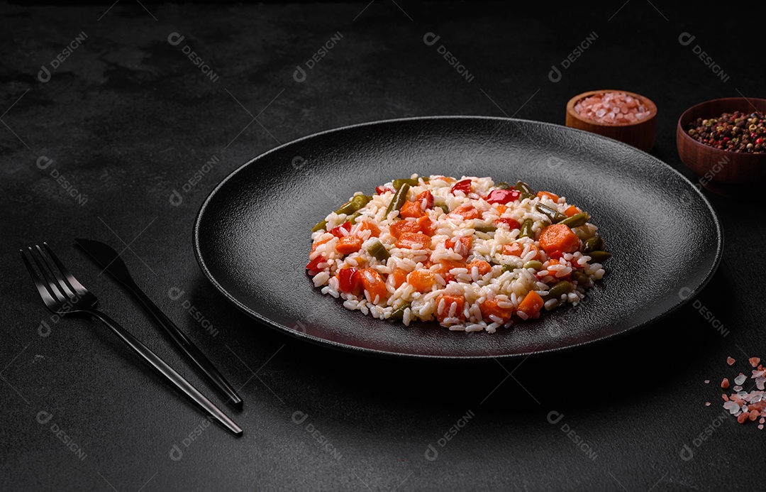 Delicioso risoto fresco com legumes, especiarias e ervas em uma placa preta sobre um fundo escuro de concreto