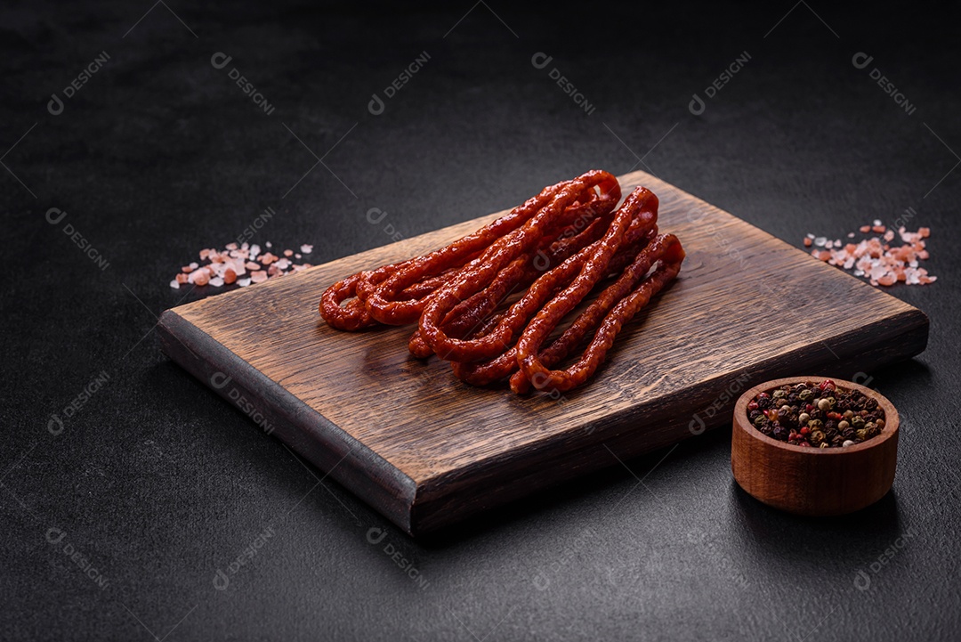 Deliciosas salsichas finas de carne fumada com especiarias e ervas sobre um fundo escuro de concreto