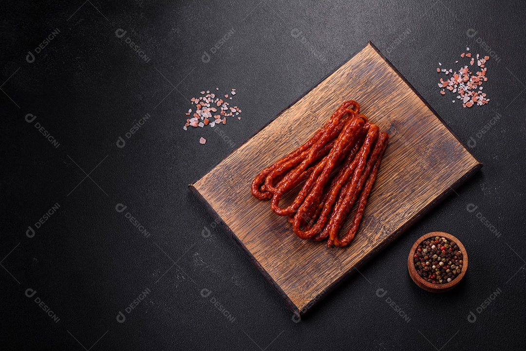 Deliciosas salsichas finas de carne fumada com especiarias e ervas sobre um fundo escuro de concreto