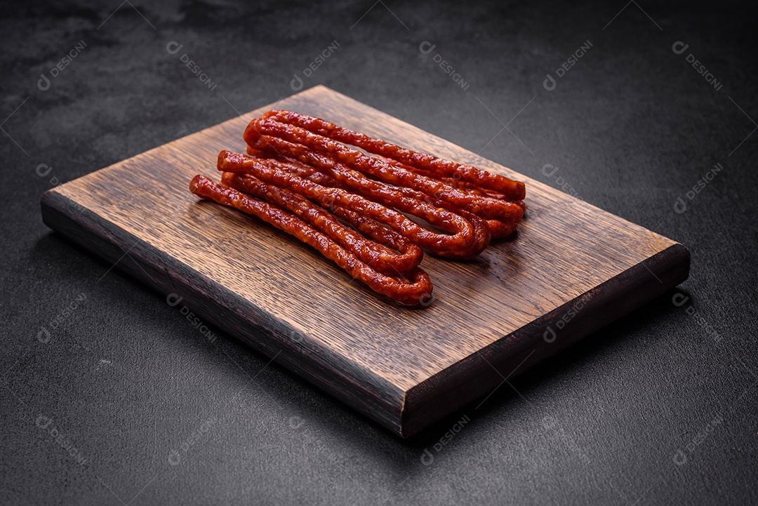 Deliciosas salsichas finas de carne fumada com especiarias e ervas sobre um fundo escuro de concreto