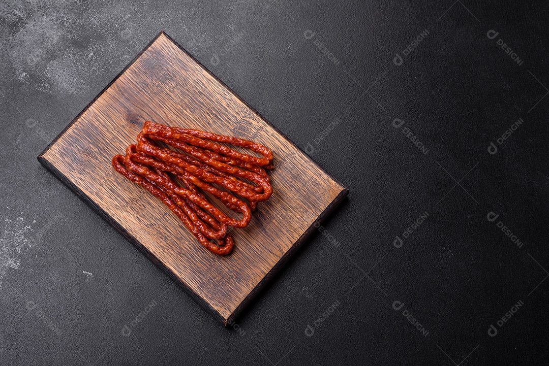 Deliciosas salsichas finas de carne fumada com especiarias e ervas sobre um fundo escuro de concreto