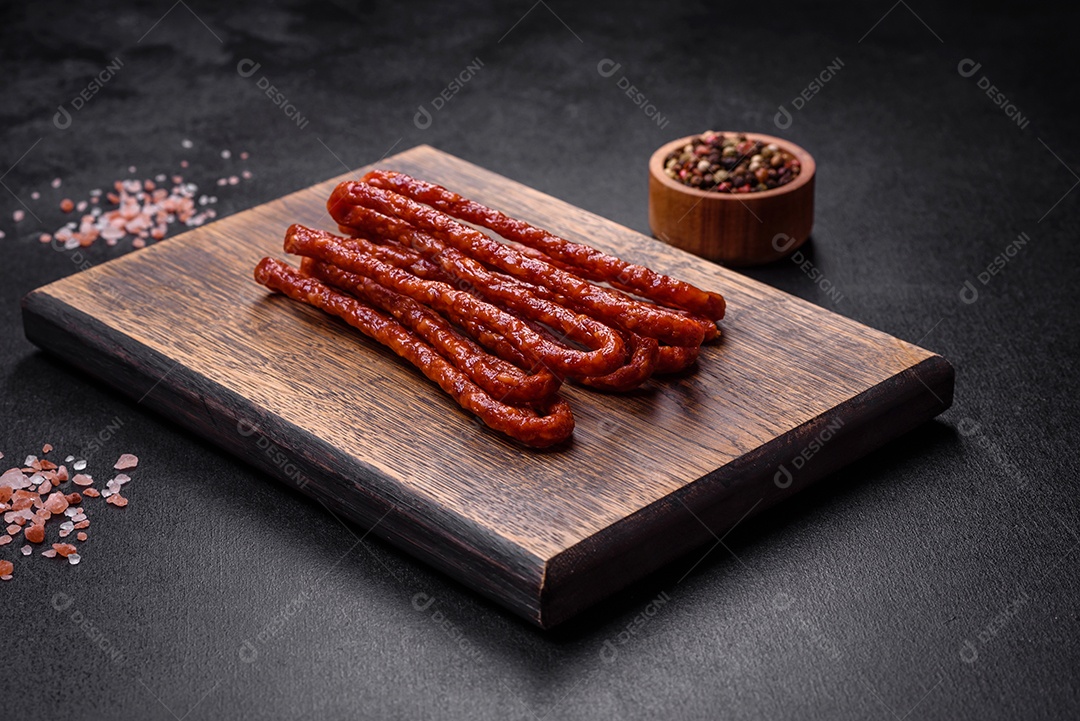 Deliciosas salsichas finas de carne fumada com especiarias e ervas sobre um fundo escuro de concreto