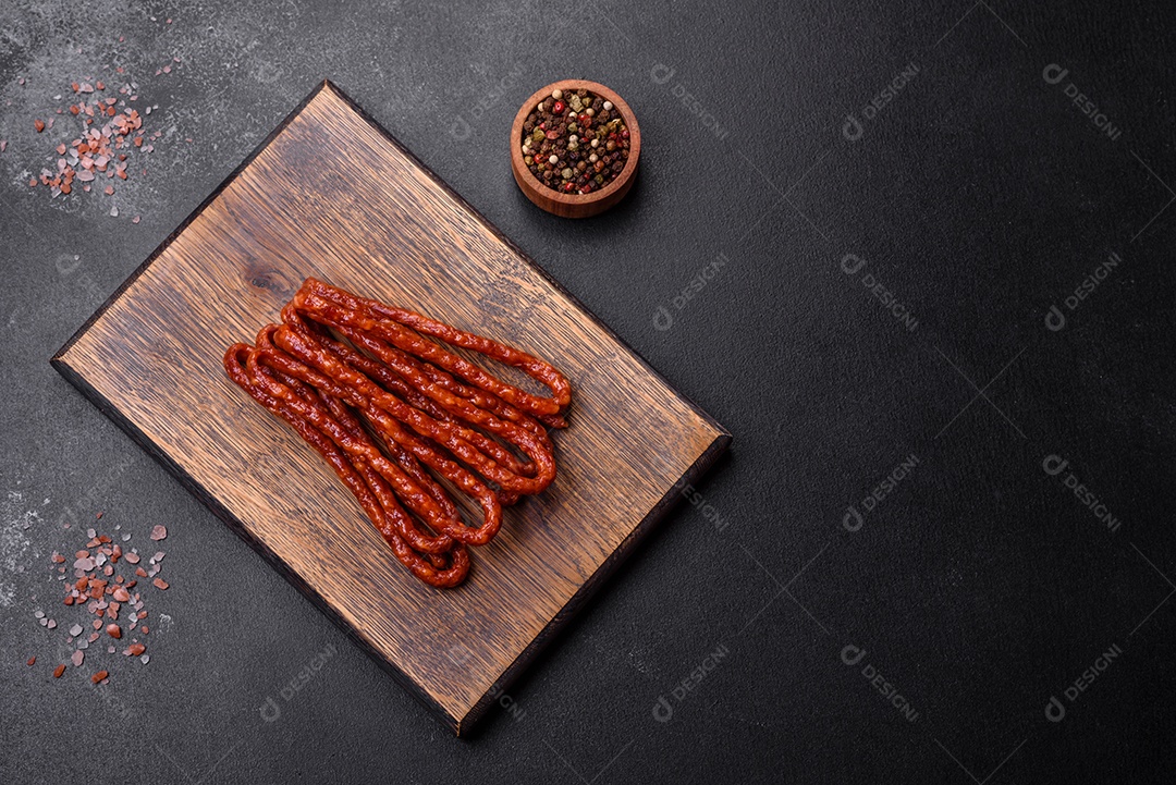 Deliciosas salsichas finas de carne fumada com especiarias e ervas sobre um fundo escuro de concreto