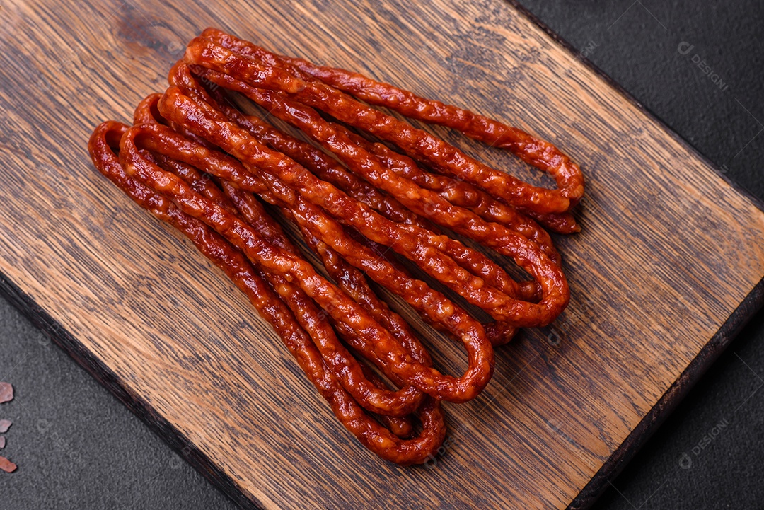 Deliciosas salsichas finas de carne fumada com especiarias e ervas sobre um fundo escuro de concreto