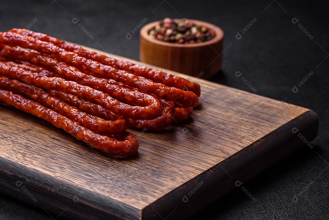 Deliciosas salsichas finas de carne fumada com especiarias e ervas sobre um fundo escuro de concreto