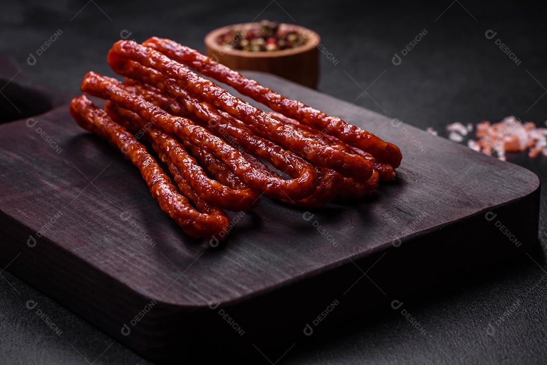 Deliciosas salsichas finas de carne fumada com especiarias e ervas sobre um fundo escuro de concreto