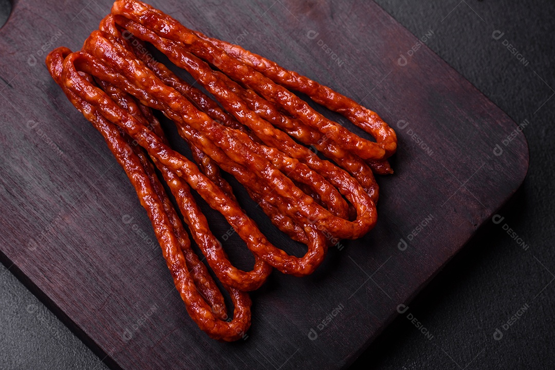 Deliciosas salsichas finas de carne fumada com especiarias e ervas sobre um fundo escuro de concreto