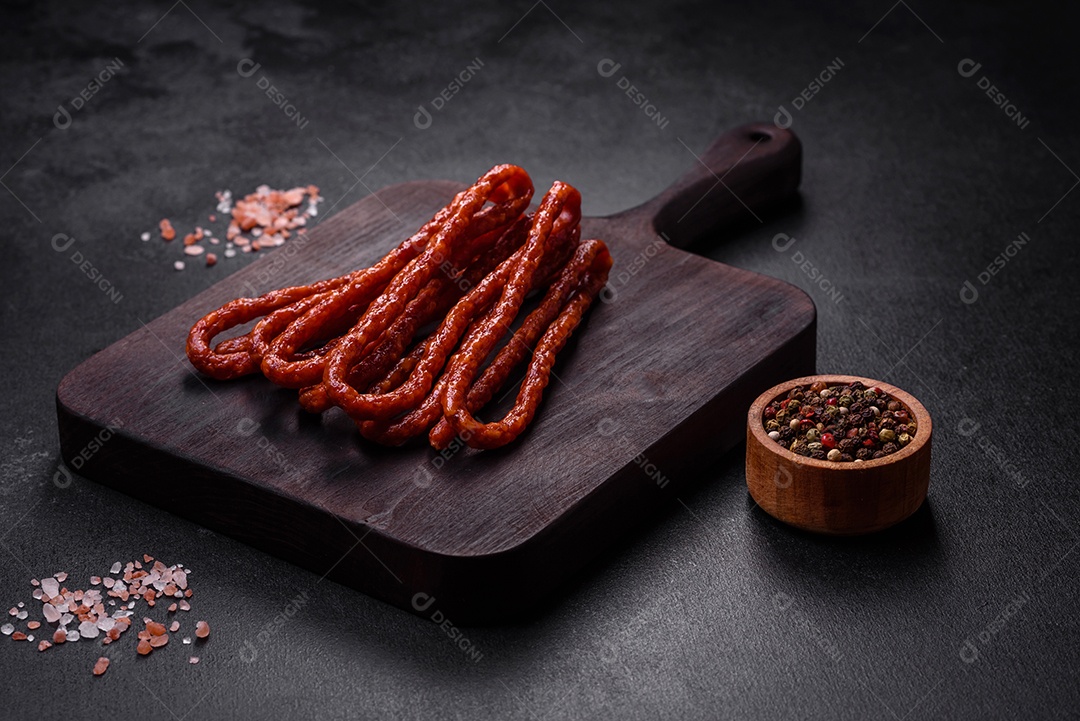 Deliciosas salsichas finas de carne fumada com especiarias e ervas sobre um fundo escuro de concreto