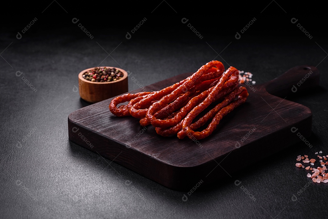 Deliciosas salsichas finas de carne fumada com especiarias e ervas sobre um fundo escuro de concreto