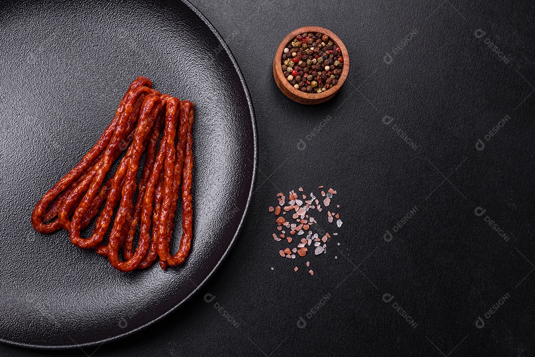 Deliciosas salsichas finas de carne fumada com especiarias e ervas sobre um fundo escuro de concreto