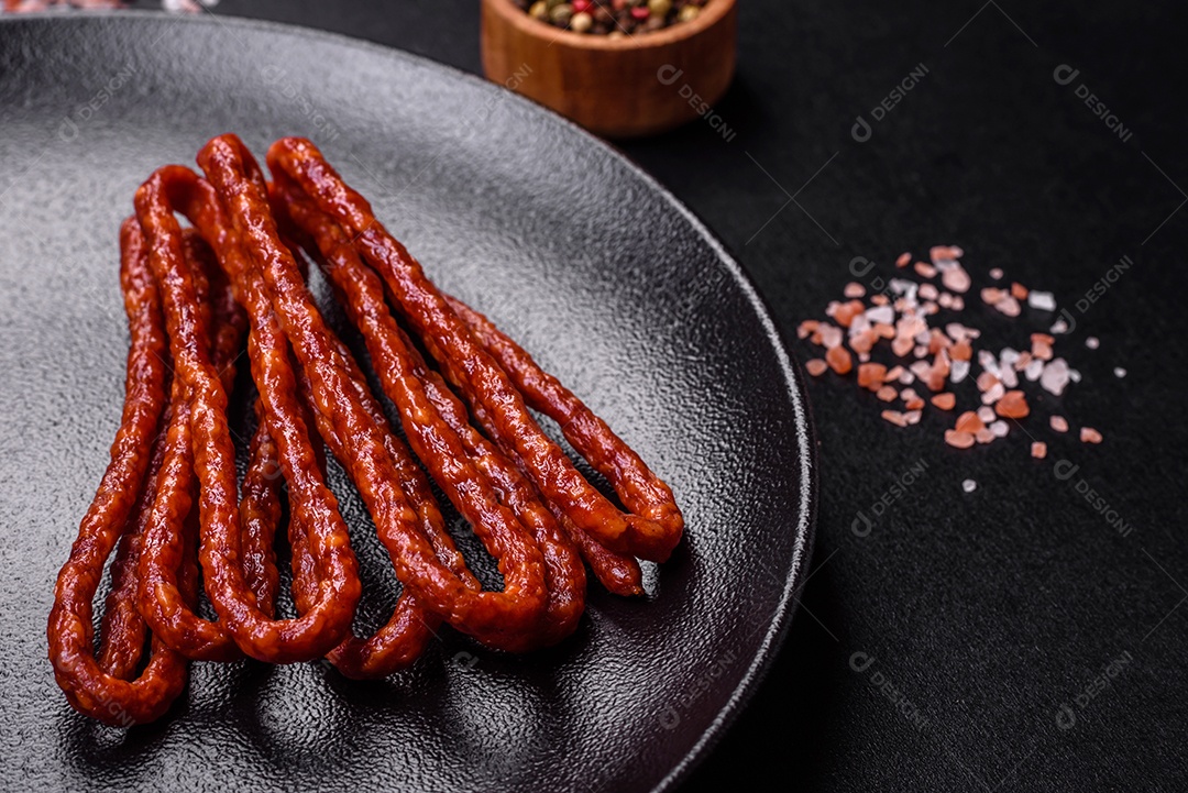 Deliciosas salsichas finas de carne fumada com especiarias e ervas sobre um fundo escuro de concreto