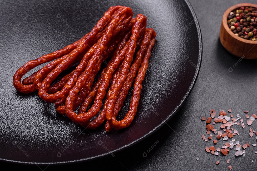 Deliciosas salsichas finas de carne fumada com especiarias e ervas sobre um fundo escuro de concreto