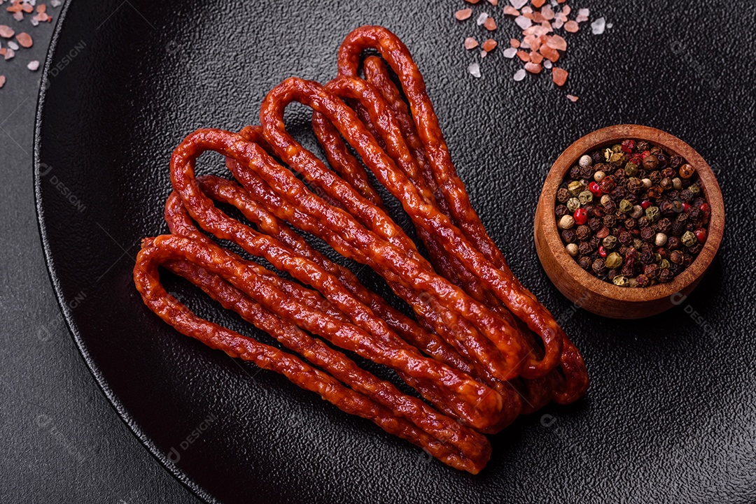 Deliciosas salsichas finas de carne fumada com especiarias e ervas sobre um fundo escuro de concreto