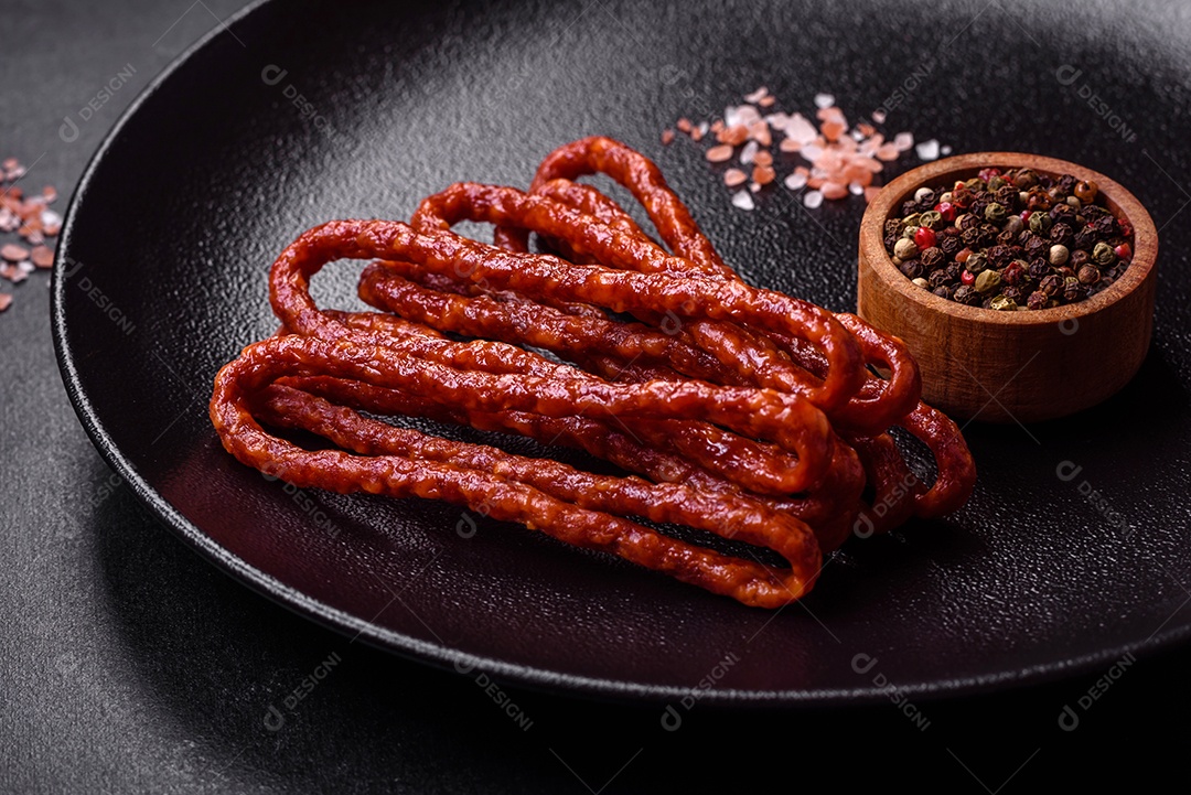 Deliciosas salsichas finas de carne fumada com especiarias e ervas sobre um fundo escuro de concreto