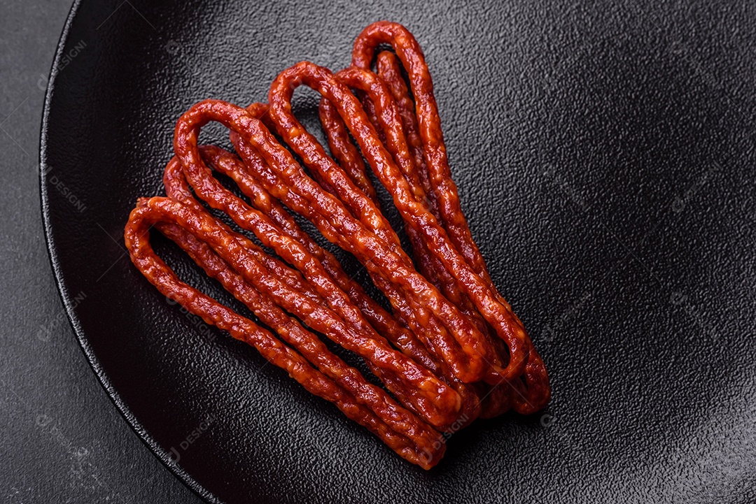 Deliciosas salsichas finas de carne fumada com especiarias e ervas sobre um fundo escuro de concreto
