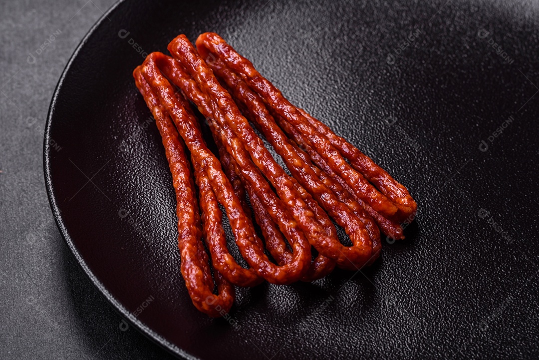 Deliciosas salsichas finas de carne fumada com especiarias e ervas sobre um fundo escuro de concreto